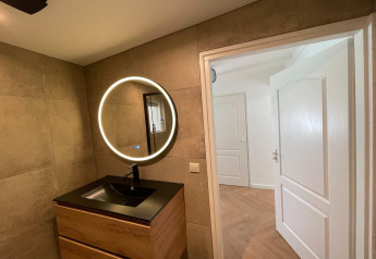 Moderne badkamer bij Forest Suite in Nederland, met ronde spiegel en houten wastafelkast onder verlichting.