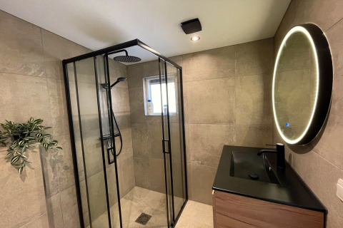 Salle de bain moderne avec douche vitrée, lavabo noir, miroir rond lumineux au Forest Suite, Pays-Bas.