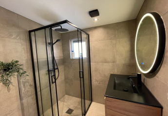 Moderne badkamer met glazen douche, zwarte wastafel, rond verlicht spiegel en plant in Forest Suite, Nederland.
