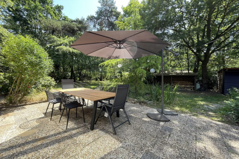 Outdoor patio at Forest suite lodge in the Netherlands with table, chairs, umbrella, and lush greenery.