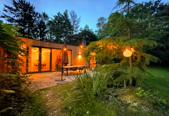 Skøn lodge ved navn Forest suite i Holland, omgivet af træer med oplyst terrasse i aftenskumringen.