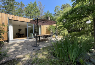 Outdoor patio at Forest suite lodge in the Netherlands with dining set, umbrella, and lush greenery.