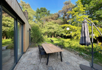 Patio view at Forest Suite lodge in the Netherlands with dining table, chairs, and lush green garden.