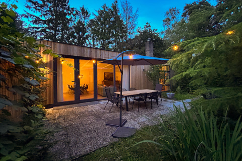 Evening view of cozy patio with dining table, umbrella and string lights at Forest Suite lodge in the Netherlands.