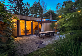 Aftenudsigt til hyggelig terrasse med spisebord, parasol og belysning ved Forest Suite-lodgen i Holland.
