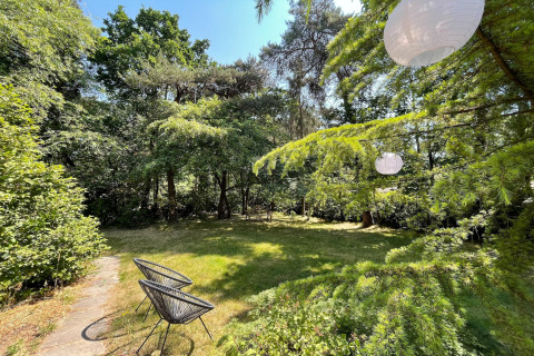 Garden with green trees, two black chairs and hanging lanterns, taken at Forest Suite lodge in the Netherlands.