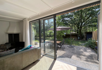 Woonkamer van Forest suite lodge in Nederland met schuifdeuren naar terras en groene tuin.