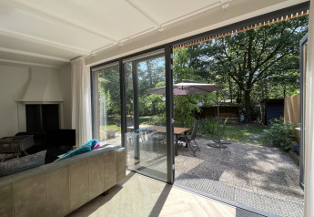 Woonkamer in Forest suite lodge Nederland, schuifdeur naar terras en bosrijke tuin.