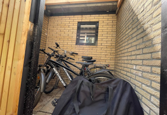 Cykler parkeret ved en væg i en lille cykelskur ved Forest Suite, Nederlandene, med en sort taske foran.