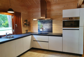 Moderne hvidt køkken med sort bordplade og trævægge, set i Casa Madeira, Holland, med skovudsigt.