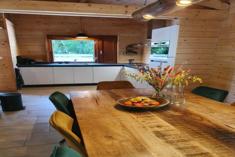 Comedor y cocina moderna con paredes de madera, flores y frutero en villa forestal de lujo en Holanda.