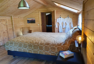 Slaapkamer in luxe bosvilla Casa Madeira in Nederland met houten interieur, tweepersoonsbed en badjassen.