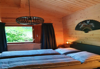 Et hyggeligt soveværelse i træ, Casa Madeira-chalet, med seng, vindue, japansk vifte og moderne lampe.