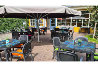 Outdoor café area at a glamping site with colorful chairs, tables, umbrellas, and small plants on tables.