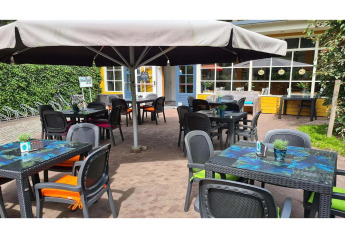 Zona de cafetería al aire libre en un glamping con sillas coloridas, mesas, sombrillas y plantas en las mesas.