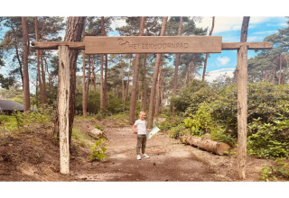 Billede af et barn under en træportal med skiltet 'Het Eekhoornpad' i en skov ved glamping.
