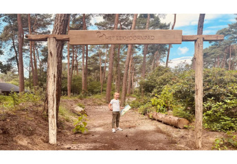 Photo of a child under a wooden 'Het Eekhoornpad' sign at the entrance of a glamping forest trail.