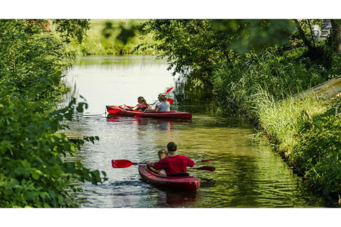 Dos kayaks rojos con familias remando en un canal rodeado de naturaleza en un alojamiento glamping.