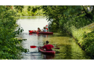 Dos kayaks rojos con familias remando en un canal rodeado de naturaleza en un alojamiento glamping.