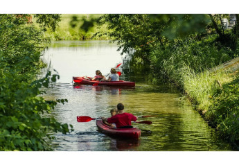 Twee rode kajaks met gezinnen peddelen op een groene gracht bij een glampingverblijf in de natuur.