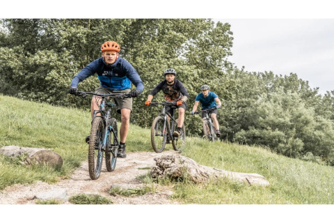 Drie personen mountainbiken op een bosparcours dichtbij een glampingverblijf, omgeven door natuur.