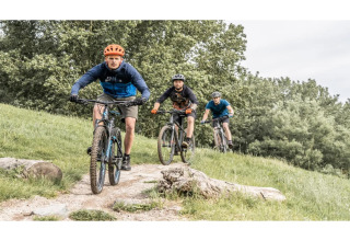 Drie personen mountainbiken op een bosparcours dichtbij een glampingverblijf, omgeven door natuur.