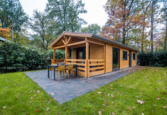 Vista exterior de una cabaña wellness para 4 personas en medio de la naturaleza con terraza y mesa en el patio.