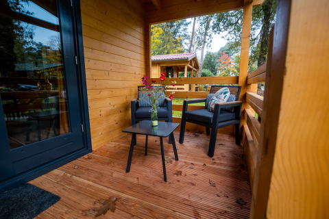 Acogedora terraza de madera con dos sillas, mesa y flores en una lodge de bienestar para 4 personas en Países Bajos.