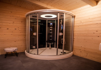 Modern round shower cabin in a wooden wellness lodge in the Netherlands, featuring warm ambient lighting.