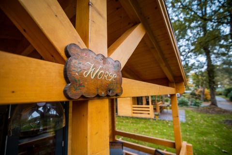 Houten bord met 'Norse' aan een wellness lodge voor 4 personen in Nederland, omgeven door groen.
