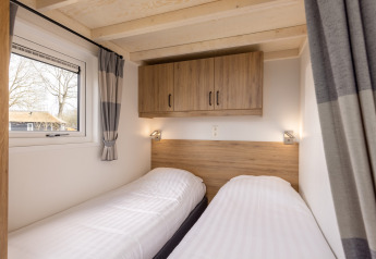 Bright bedroom with two single beds, wooden cabinets and window in tiny house at Holiday Park Tolplas 19.