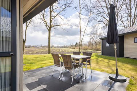 Outdoor patio at Holiday park Tolplas 19 with table, chairs, umbrella, and scenic Dutch countryside view.