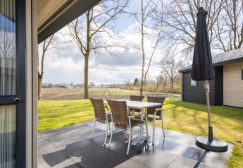 Outdoor patio at Holiday park Tolplas 19 with table, chairs, umbrella, and scenic Dutch countryside view.