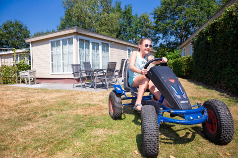 Pige kører på pedalbil foran et lille sommerhus i Holiday park «Tolplas 19» i Holland på en solskinsdag.