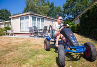 Niña conduciendo un coche de pedales frente a una tiny house en Holiday park «Tolplas 19» en Países Bajos.