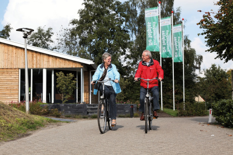 Senior couple cycling in front of a wooden cabin at Holiday park Tolplas 19 in the Netherlands.