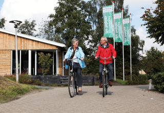 Couple de seniors à vélo devant un chalet au parc de vacances Tolplas 19 aux Pays-Bas.