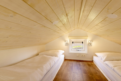 Dos camas individuales en una buhardilla con techo de madera y ventana pequeña en Tolplas 19, Países Bajos.