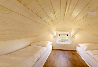 Two single beds in an attic room with wood ceiling and small window in Holiday park Tolplas 19 tiny house.
