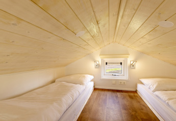 Two single beds in an attic room with wood ceiling and small window in Holiday park Tolplas 19 tiny house.