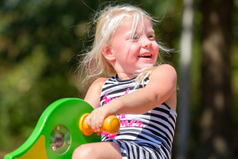 A blonde girl joyfully plays outdoors at the Holiday park Tolplas 19 in the Netherlands on a sunny day.
