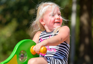 Blondes Mädchen spielt fröhlich draußen im Ferienpark Tolplas 19 in den Niederlanden bei Sonne.