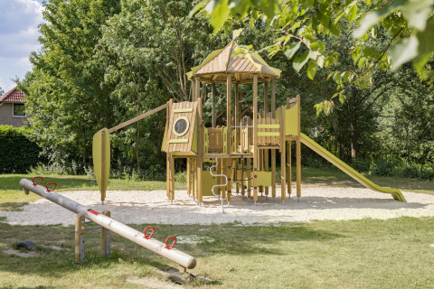 Parco giochi con scivolo e altalena presso Holiday Park Tolplas 19, circondato da alberi nei Paesi Bassi.