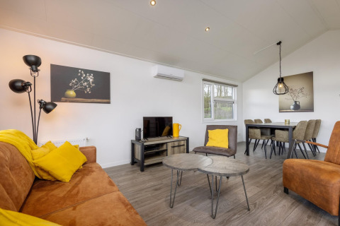 Lyst og moderne opholdsområde i feriepark Tolplas 18 i Holland, med gule puder og elegant indretning.