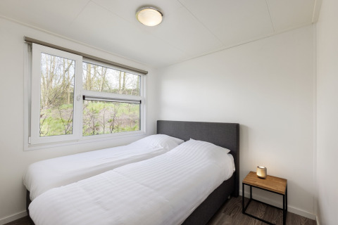 Camera da letto con due letti singoli, biancheria bianca, comodino e finestra a Holiday park Tolplas 18, Paesi Bassi.