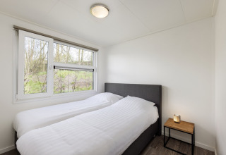 Schlafzimmer mit zwei Einzelbetten, weißer Bettwäsche, Nachttisch und Fenster im Ferienpark Tolplas 18, Niederlande.