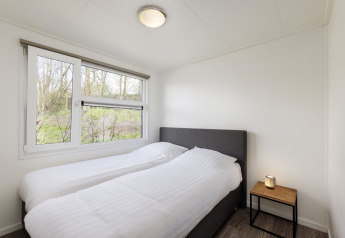 Bedroom with two single beds, white bedding, nightstand, and window at Holiday park Tolplas 18 in the Netherlands.