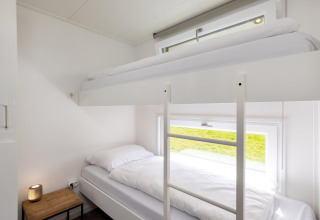 Moderne køjeseng med hvide lagner i et lyst værelse på Holiday park «Tolplas 18» i Nederlandene.