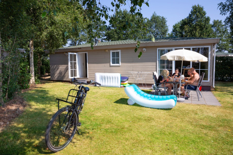 En familie nyder frokost udenfor en lille feriebolig i Tolplas 19, Nederlandene, med cykel og oppustelig stol.