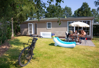 A family enjoys lunch outside a tiny house at Holiday Park Tolplas 19 in the Netherlands, with a bike nearby.